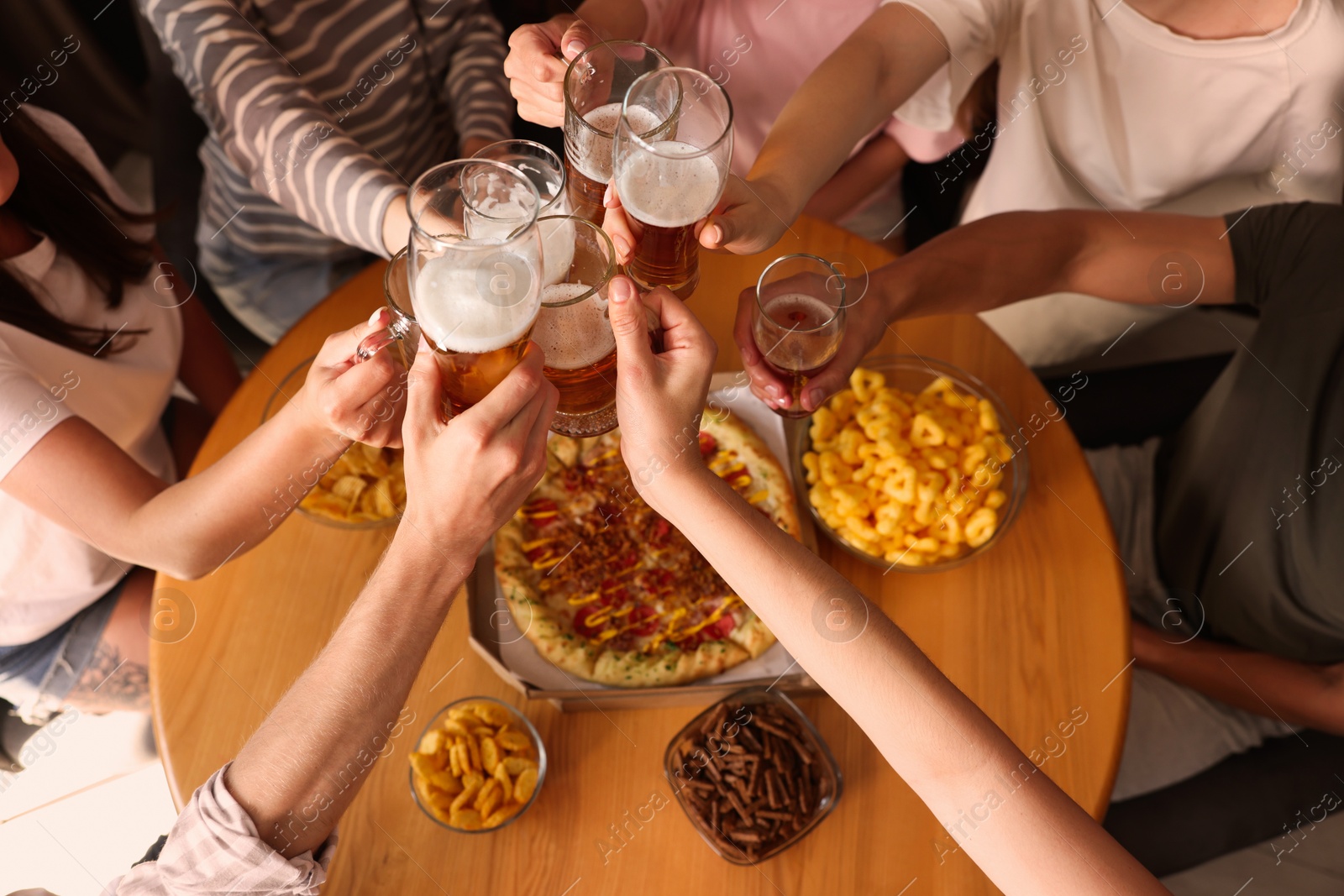 Photo of Group of happy friends clinking glasses of beer at table indoors, above view