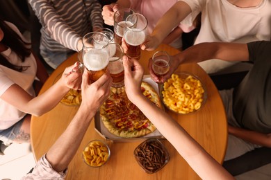 Photo of Group of happy friends clinking glasses of beer at table indoors, above view