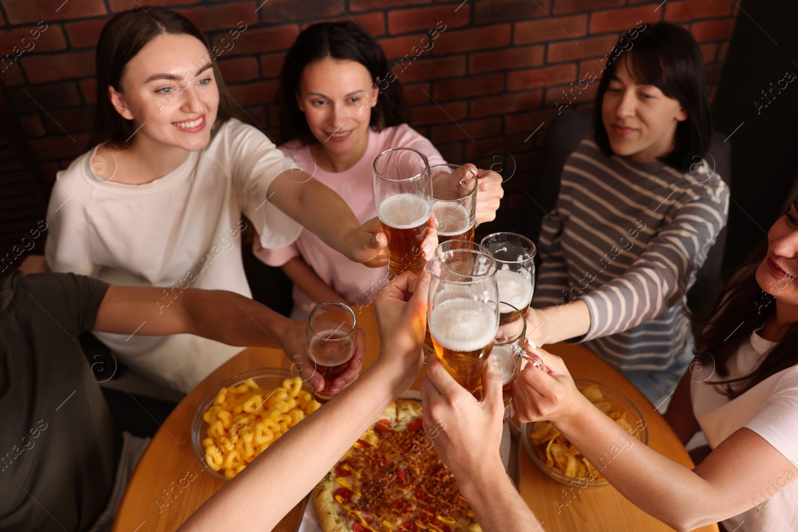 Photo of Group of happy friends clinking glasses of beer at table indoors, above view