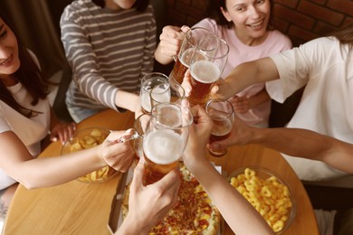 Photo of Group of happy friends clinking glasses of beer at table indoors, above view