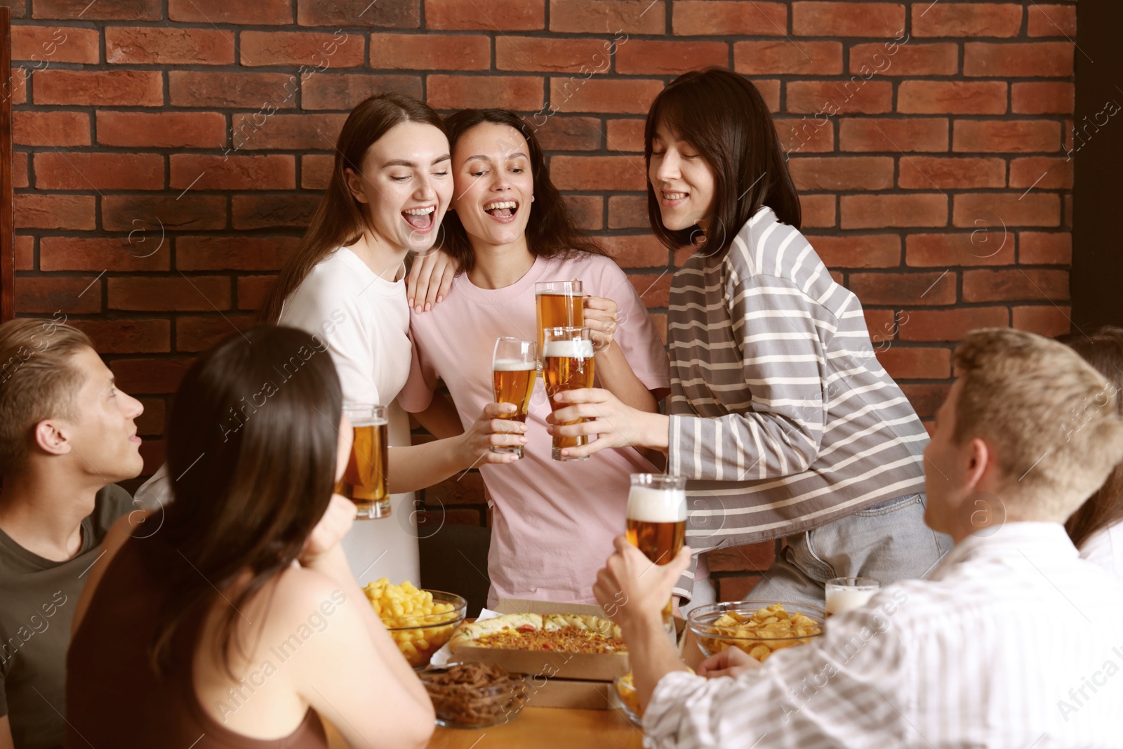 Photo of Group of happy friends clinking glasses of beer at table indoors