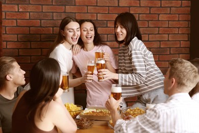 Photo of Group of happy friends clinking glasses of beer at table indoors