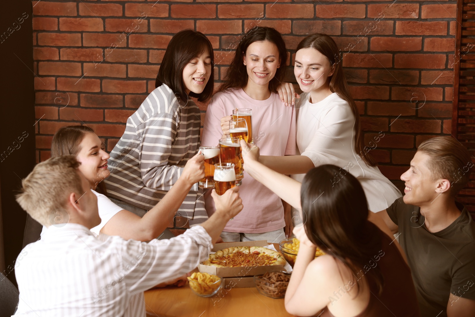 Photo of Group of happy friends clinking glasses of beer at table indoors