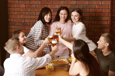 Photo of Group of happy friends clinking glasses of beer at table indoors