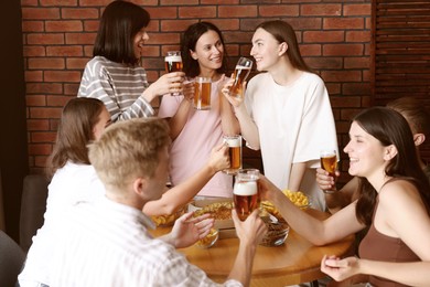 Photo of Group of friends with beer and snacks having fun at wooden table indoors