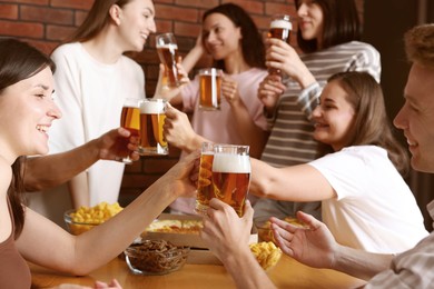 Photo of Group of happy friends clinking glasses of beer at table indoors, selective focus