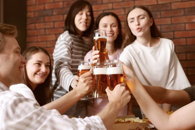 Photo of Group of happy friends clinking glasses of beer at table indoors, selective focus