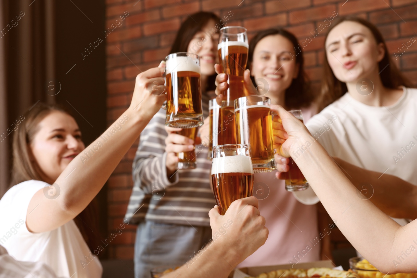Photo of Group of happy friends clinking glasses of beer at table indoors, selective focus