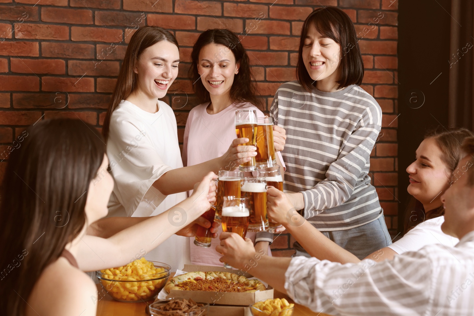 Photo of Group of happy friends clinking glasses of beer at table indoors