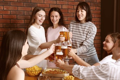 Photo of Group of happy friends clinking glasses of beer at table indoors