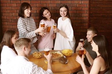 Photo of Group of happy friends clinking glasses of beer at table indoors