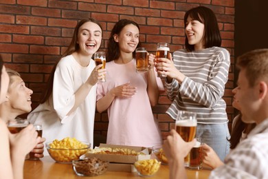 Photo of Group of friends with beer and snacks having fun at wooden table indoors