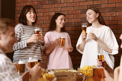 Photo of Group of friends with beer and snacks having fun at wooden table indoors