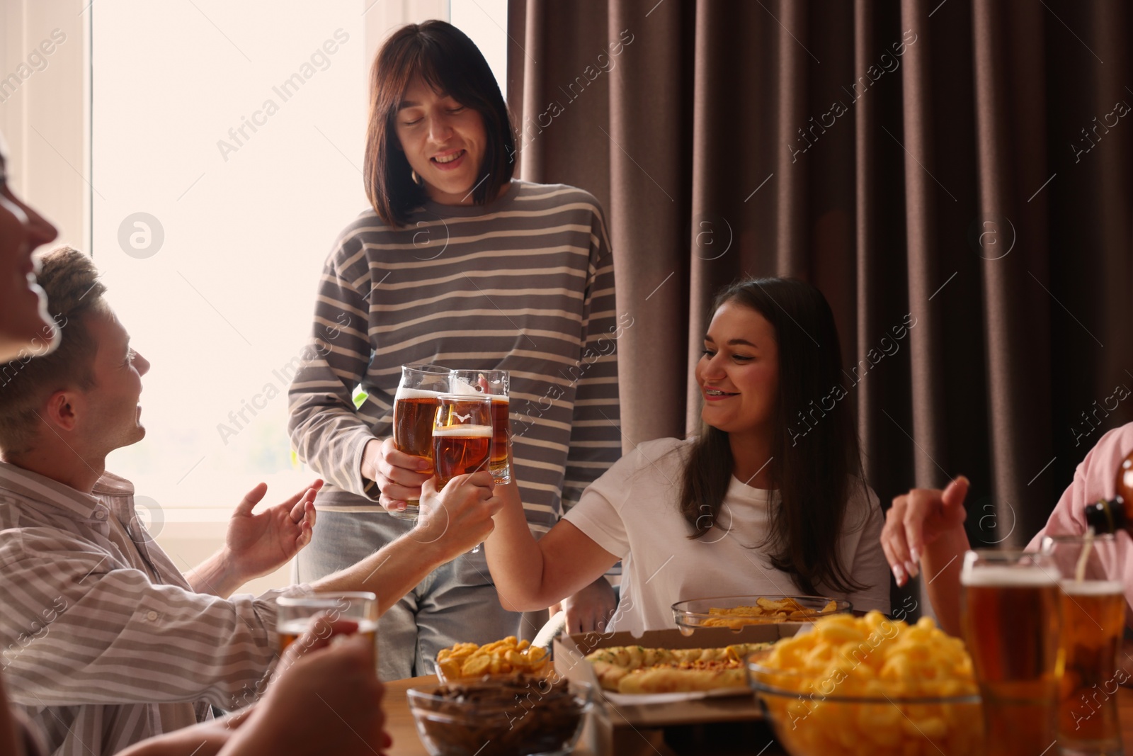 Photo of Group of happy friends clinking glasses of beer at table indoors