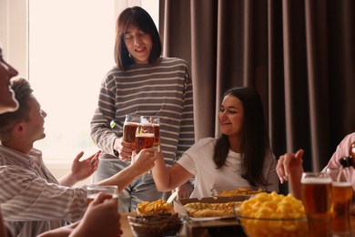 Photo of Group of happy friends clinking glasses of beer at table indoors