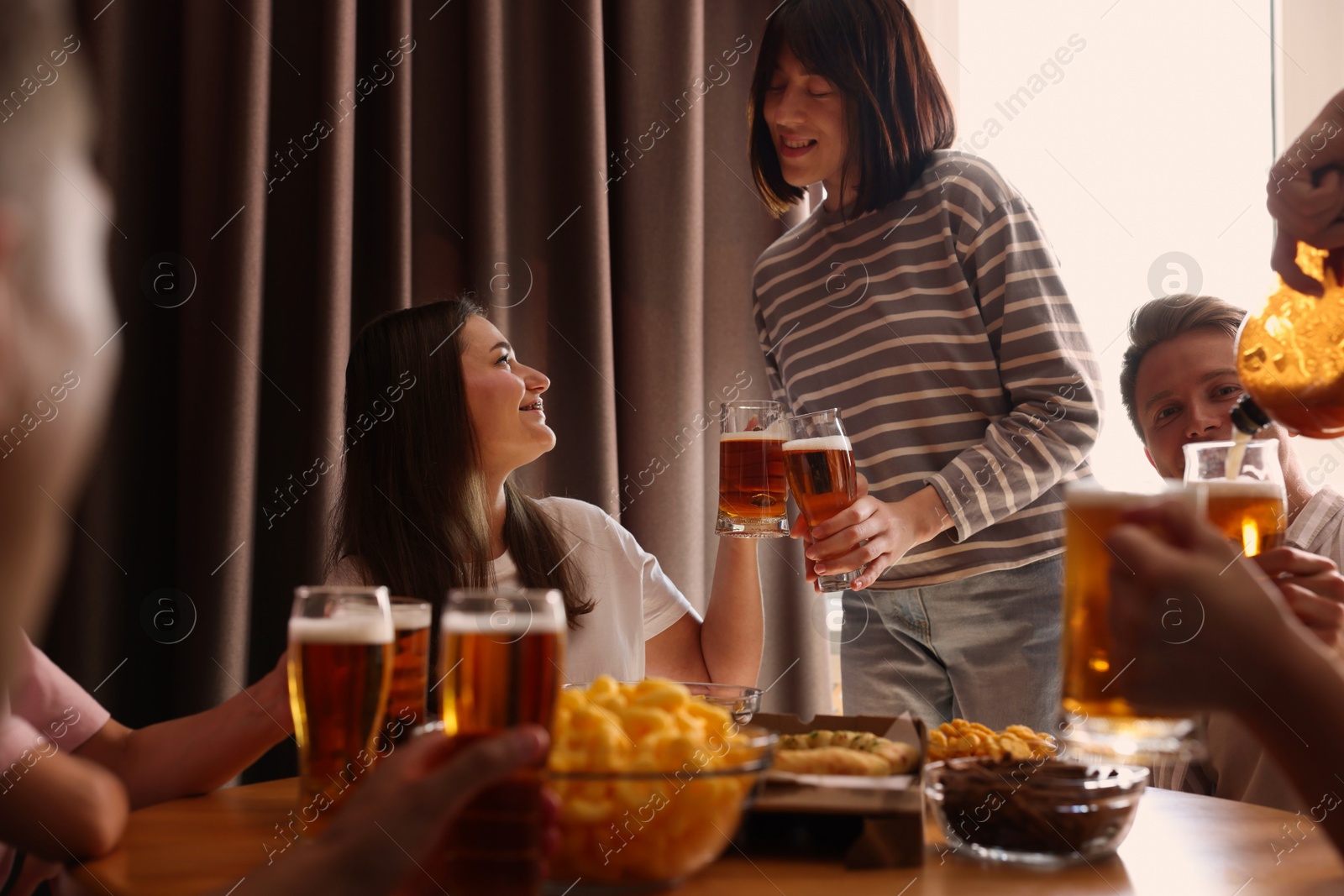 Photo of Group of happy friends clinking glasses of beer at table indoors