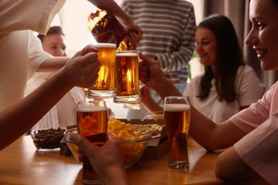 Photo of Group of happy friends clinking glasses of beer at table indoors, selective focus