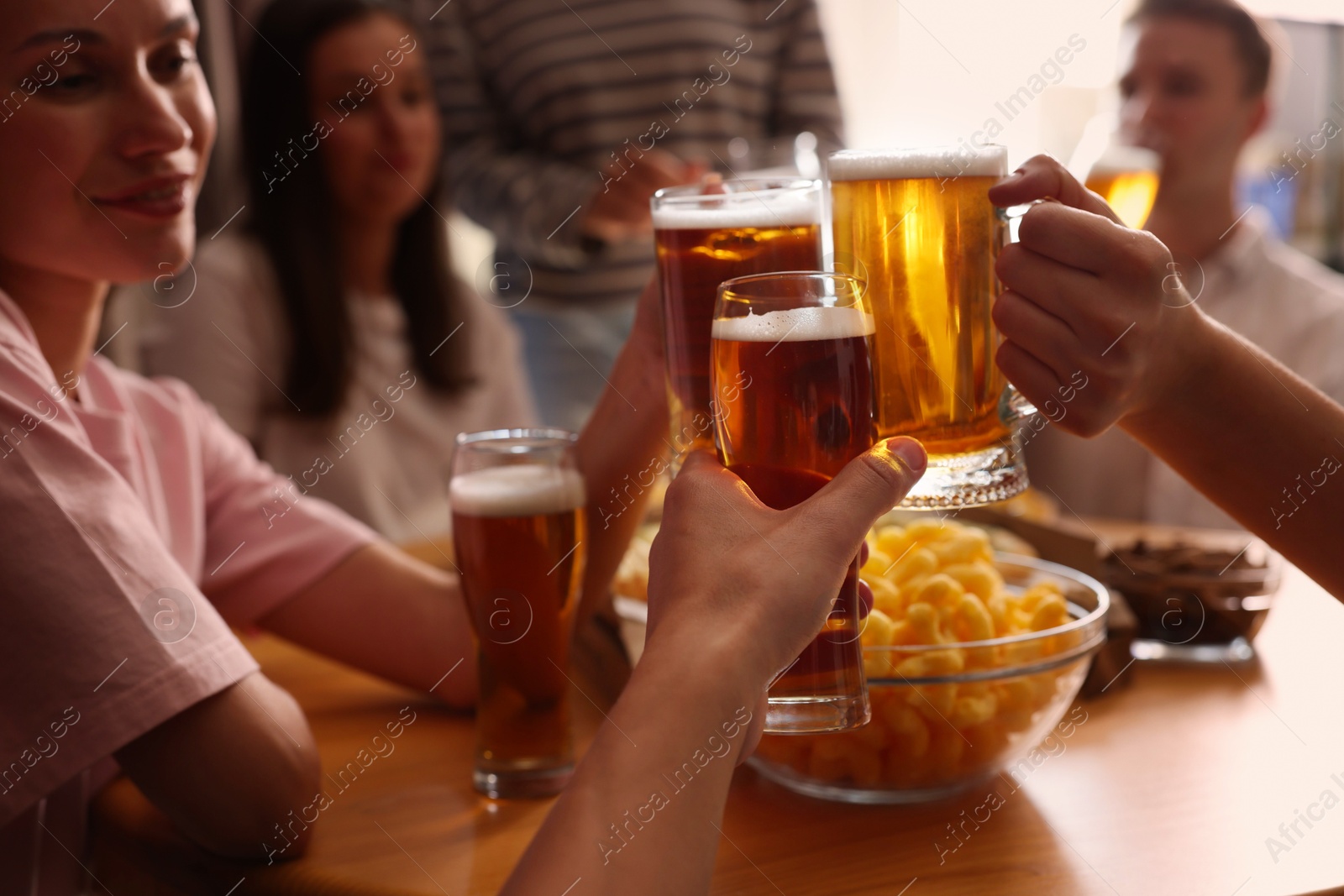 Photo of Group of happy friends clinking glasses of beer at table indoors, selective focus