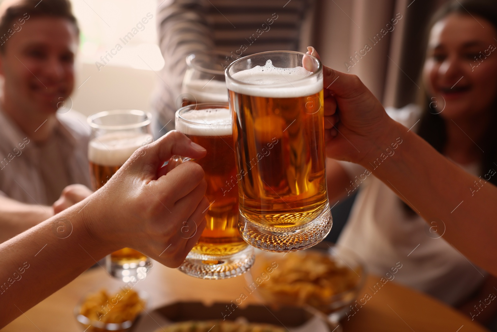 Photo of Group of happy friends clinking glasses of beer at table indoors, selective focus