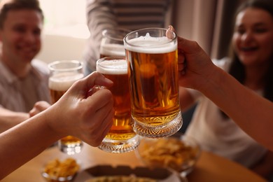 Photo of Group of happy friends clinking glasses of beer at table indoors, selective focus