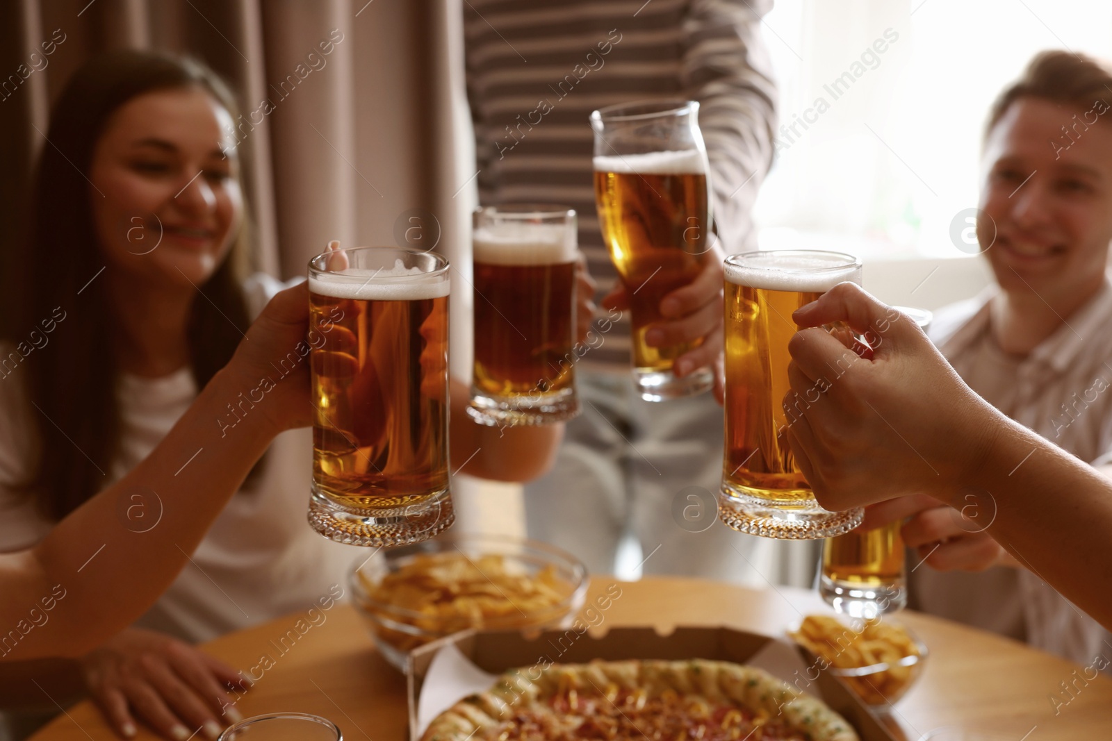 Photo of Group of happy friends clinking glasses of beer at table indoors, selective focus