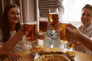 Photo of Group of happy friends clinking glasses of beer at table indoors, selective focus