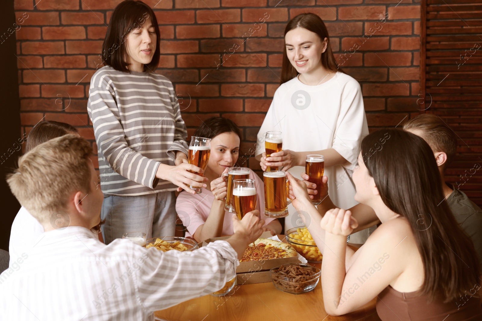 Photo of Group of happy friends clinking glasses of beer at table indoors