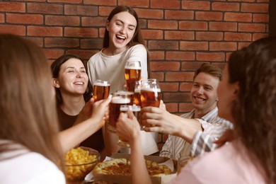 Photo of Group of happy friends clinking glasses of beer at table indoors