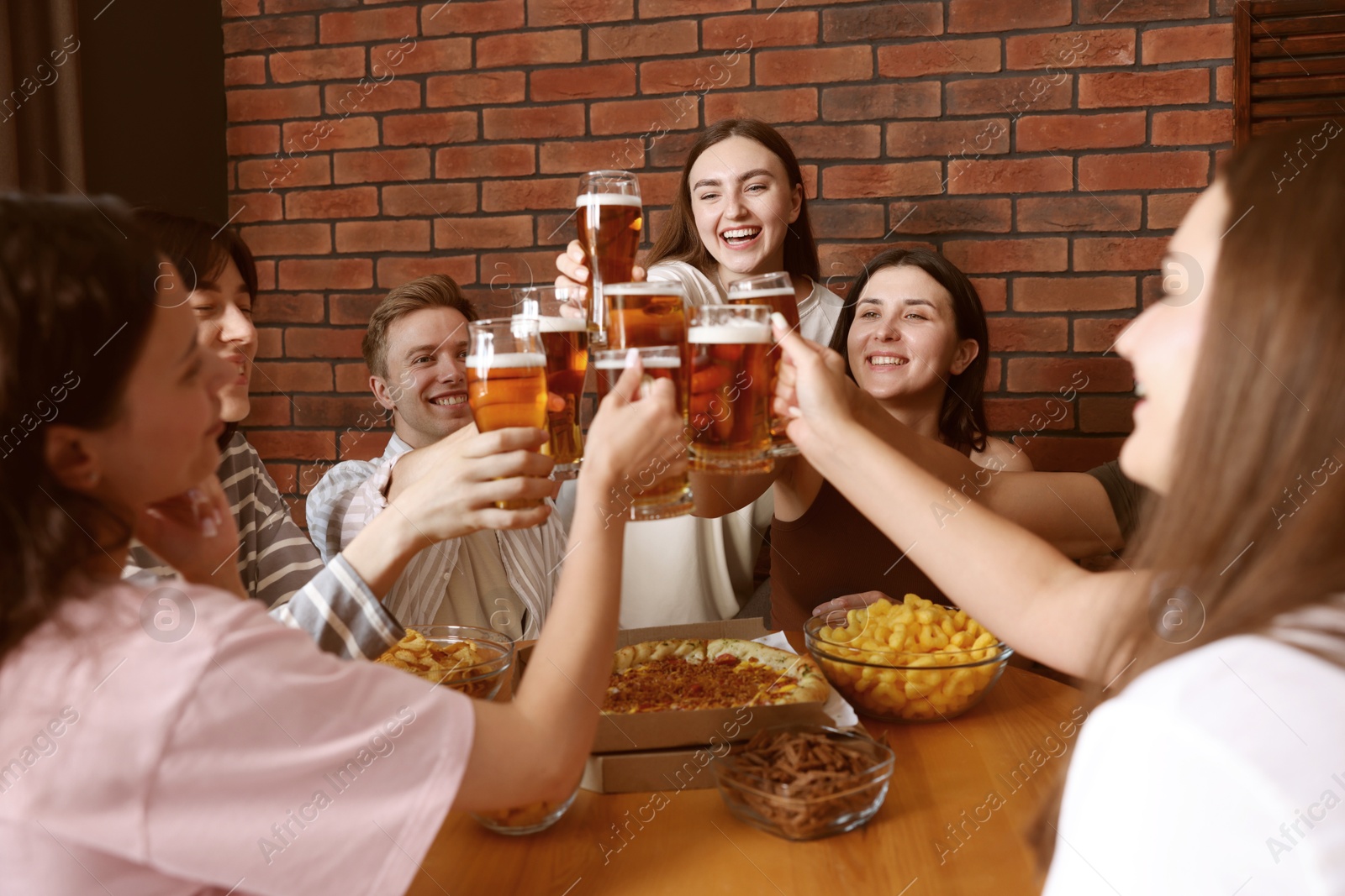 Photo of Group of happy friends clinking glasses of beer at table indoors