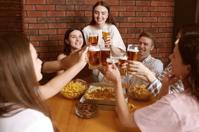 Photo of Group of happy friends clinking glasses of beer at table indoors