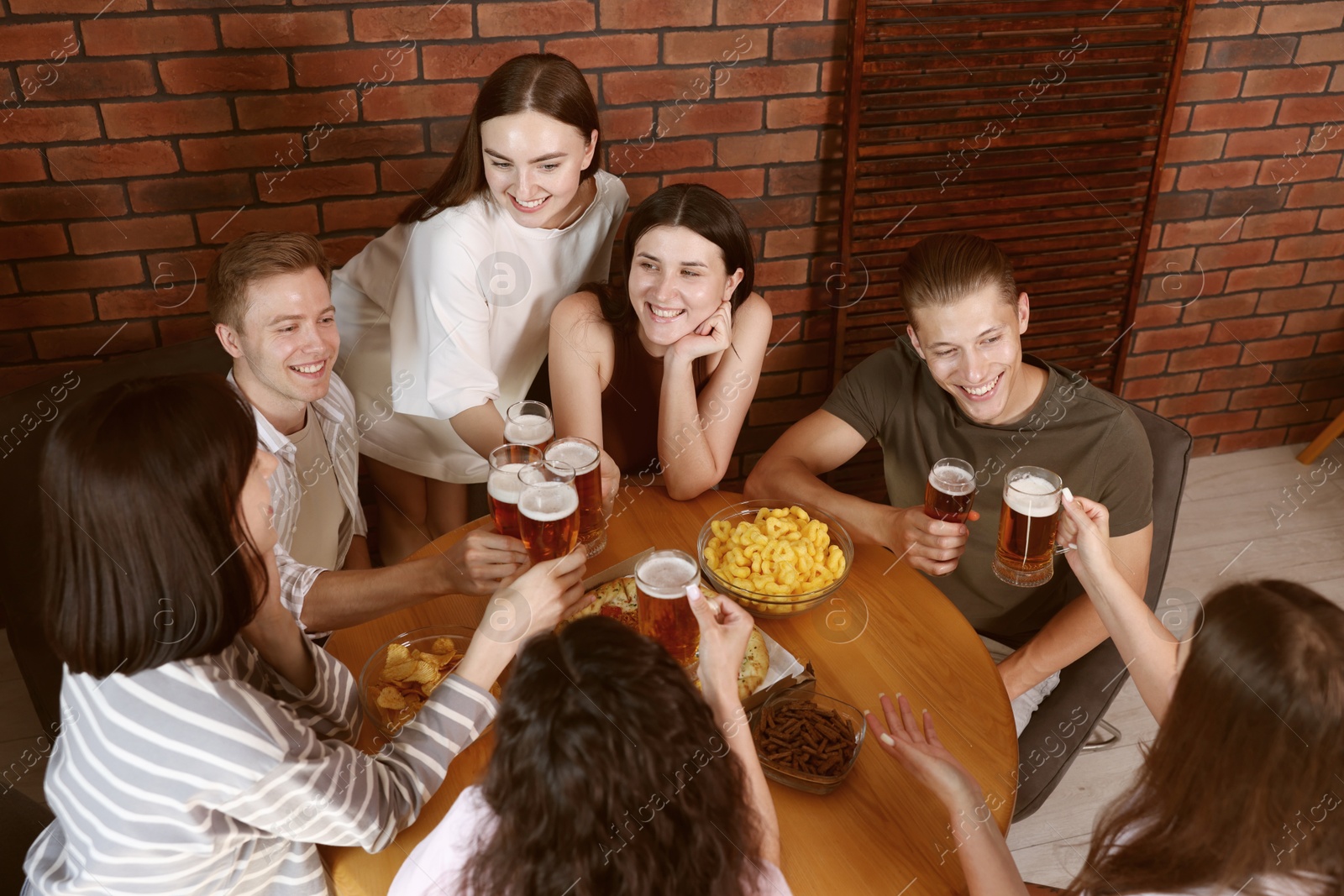 Photo of Group of friends with beer and snacks having fun at wooden table indoors, above view