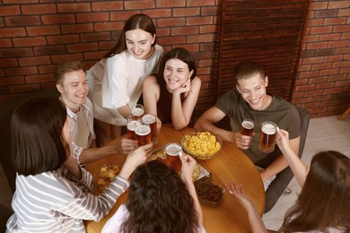 Photo of Group of friends with beer and snacks having fun at wooden table indoors, above view