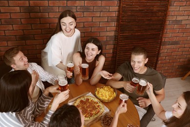 Photo of Group of friends with beer and snacks having fun at wooden table indoors, above view