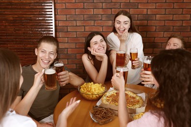 Photo of Group of friends with beer and snacks having fun at wooden table indoors