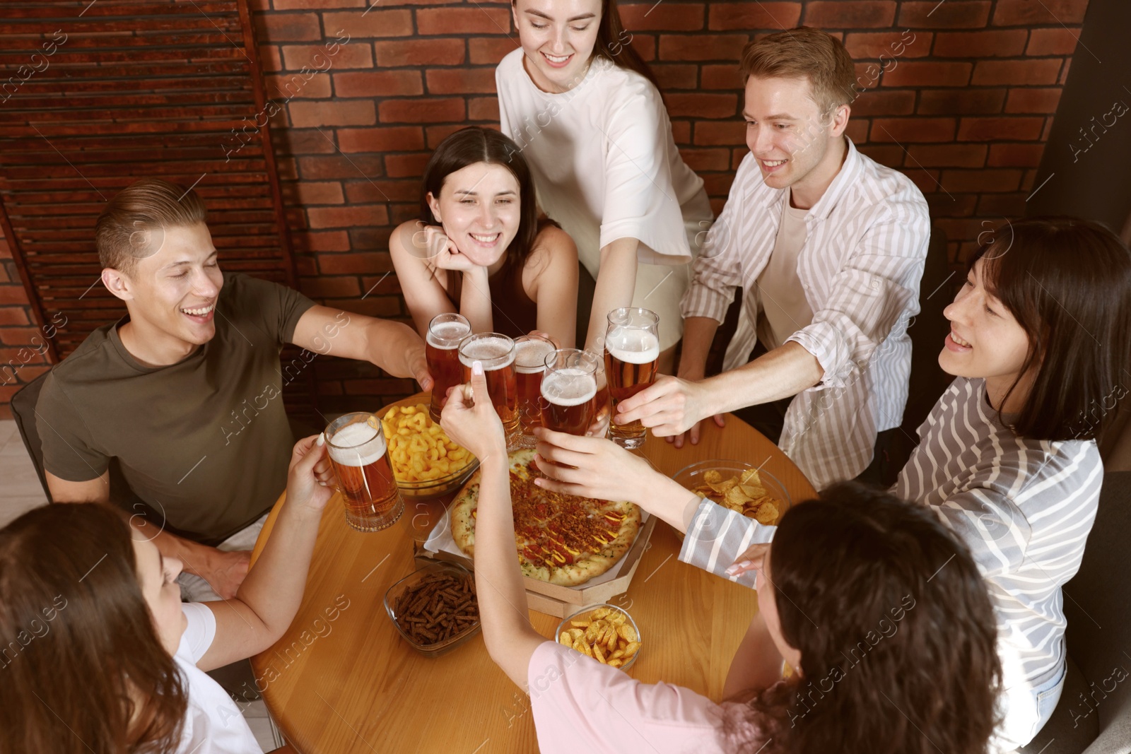 Photo of Group of happy friends clinking glasses of beer at table indoors