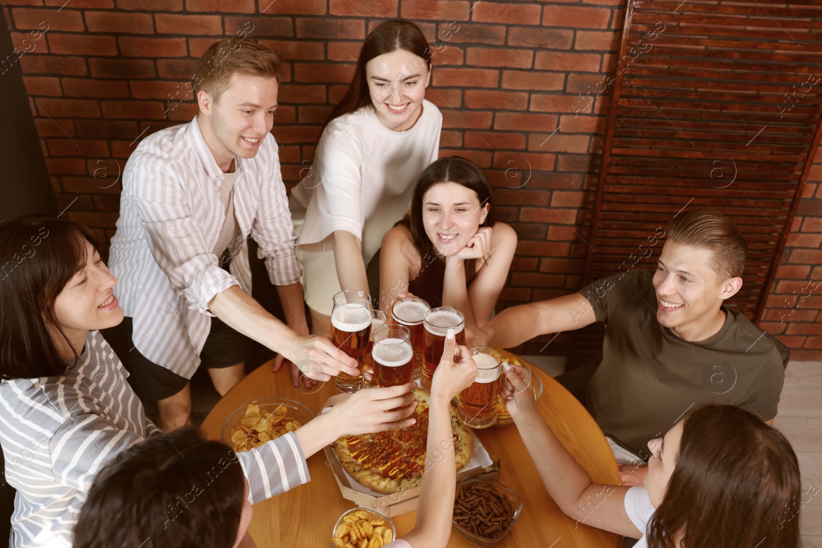 Photo of Group of happy friends clinking glasses of beer at table indoors