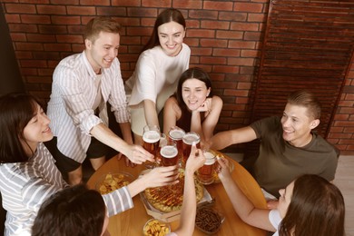 Photo of Group of happy friends clinking glasses of beer at table indoors