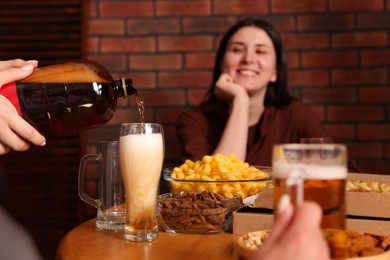 Photo of Woman pouring beer into glass at wooden table indoors, selective focus