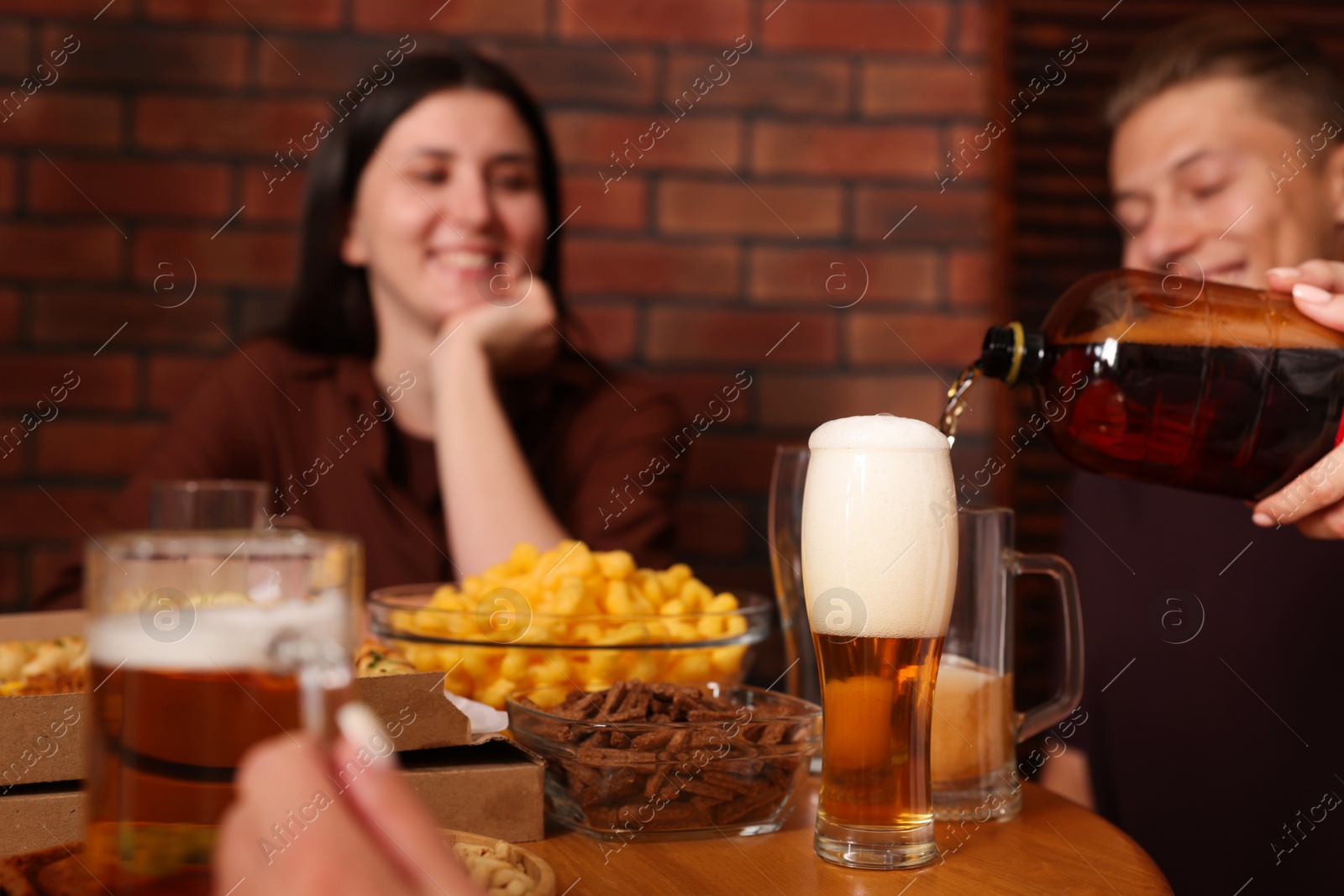Photo of Woman pouring beer into glass at wooden table indoors, selective focus
