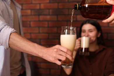 Photo of Young woman pouring beer into glass indoors, selective focus