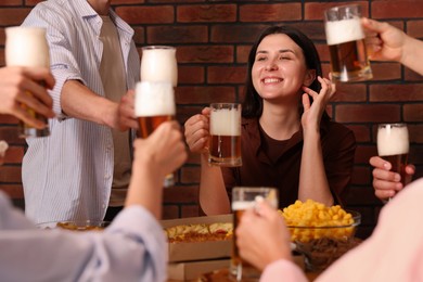 Photo of Group of happy friends clinking glasses of beer at table indoors