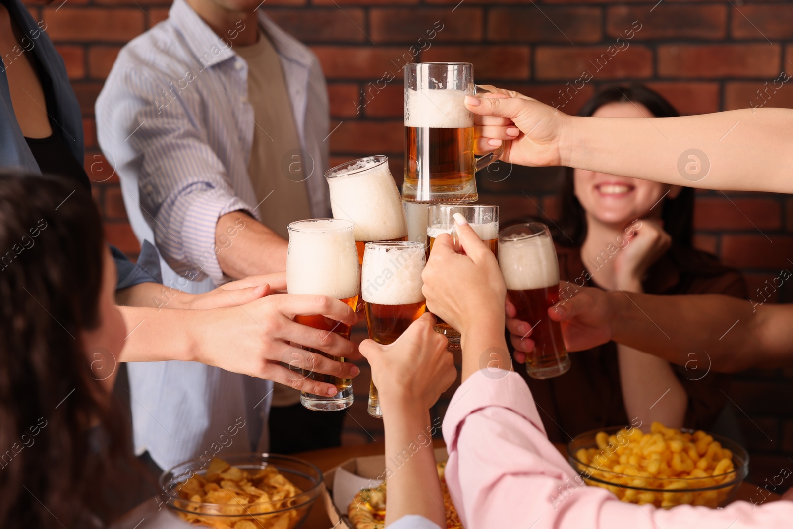 Photo of Group of happy friends clinking glasses of beer at table indoors, closeup