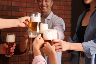 Photo of Group of happy friends clinking glasses of beer at table indoors, selective focus