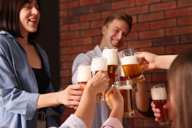 Photo of Group of happy friends clinking glasses of beer at table indoors, selective focus