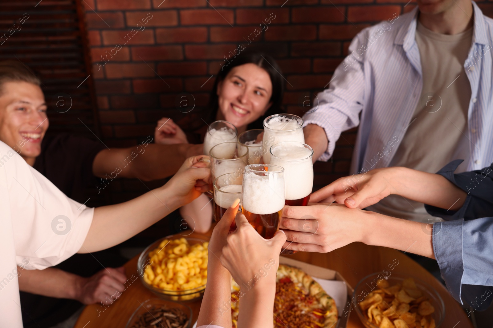 Photo of Group of happy friends clinking glasses of beer at table indoors, selective focus