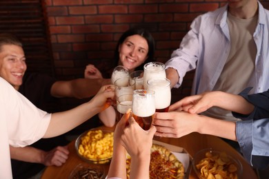 Photo of Group of happy friends clinking glasses of beer at table indoors, selective focus