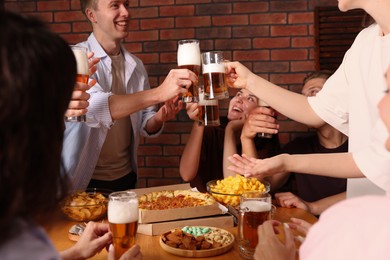Photo of Group of happy friends clinking glasses of beer at table indoors