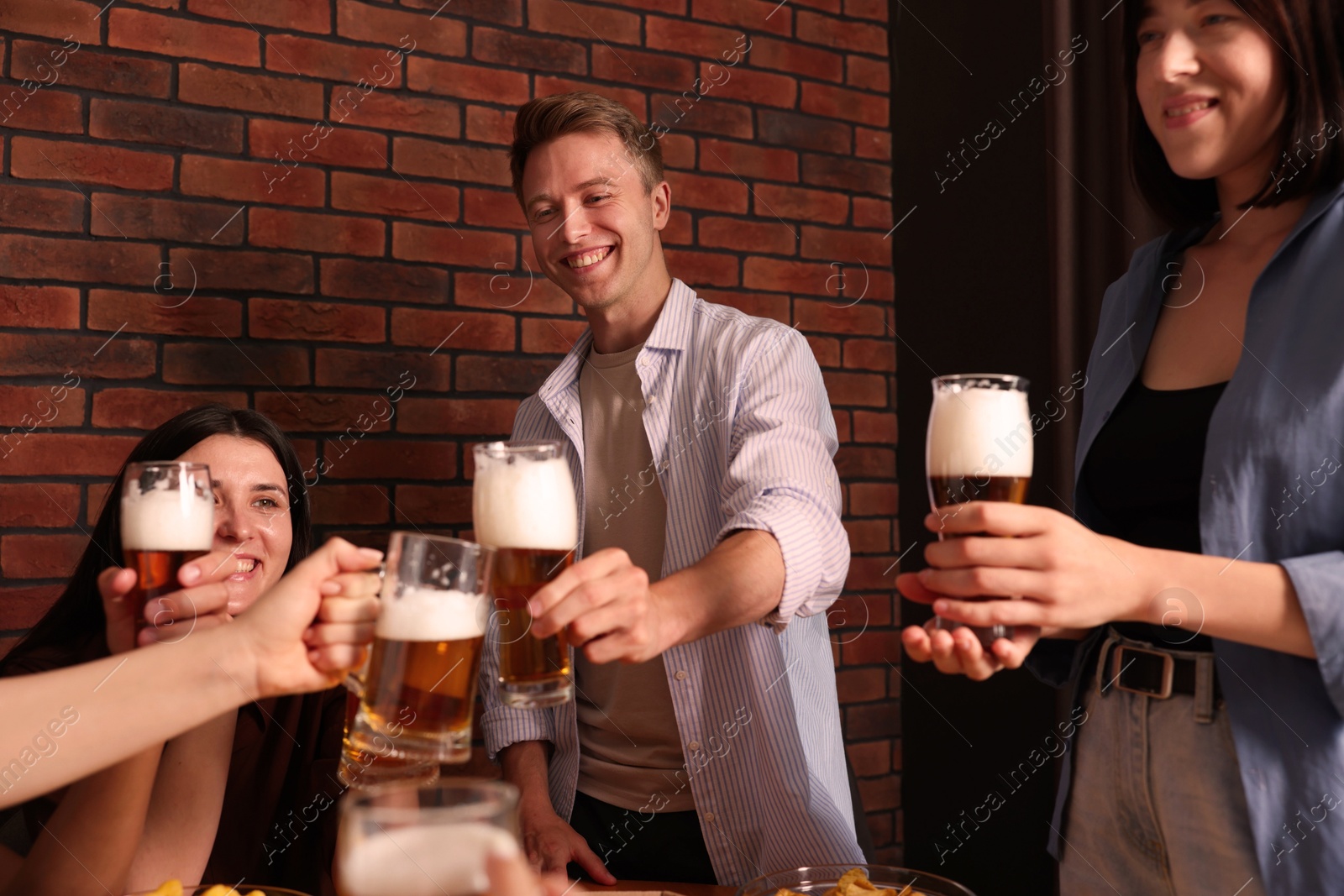 Photo of Group of happy friends clinking glasses of beer at table indoors