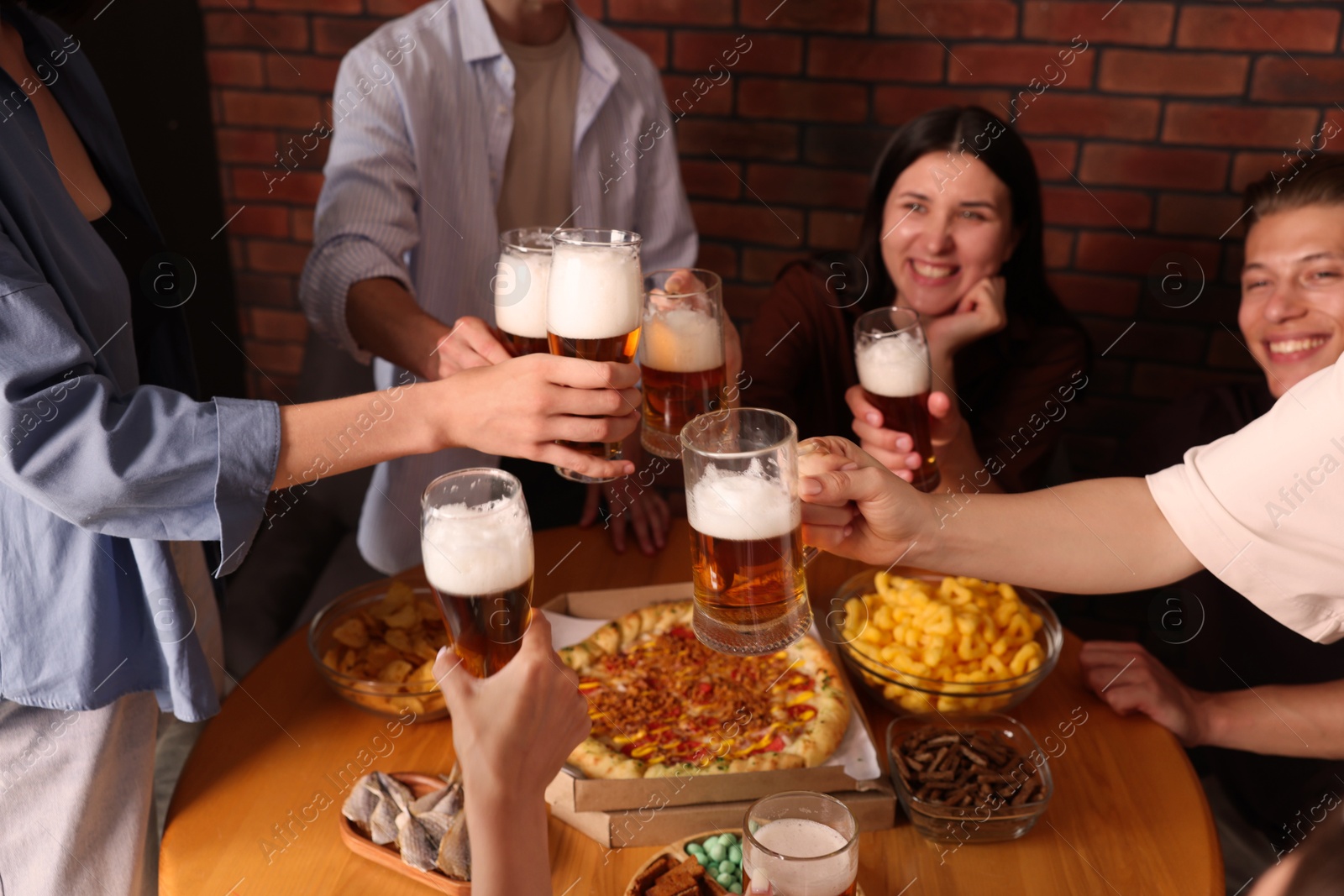 Photo of Group of happy friends clinking glasses of beer at table indoors, selective focus