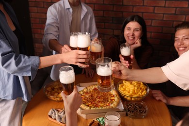 Photo of Group of happy friends clinking glasses of beer at table indoors, selective focus